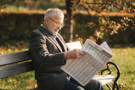 戴眼镜的白发老人一位老人在公园里看报纸的画像