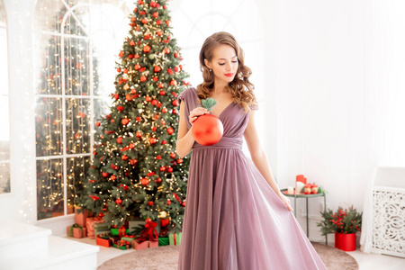 圣诞树装饰，美丽的女孩手里拿着红球，窗外的灯光。晚礼服概念派对