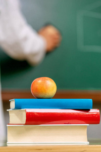 Closeup view, of a teacher desk with a pile of books and a red a