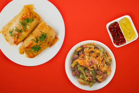  cabbage rolls in a white plate with vegetable salad and sauce. 