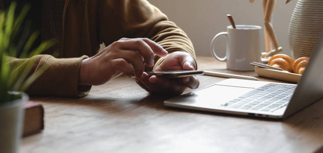 Cropped shot of young man using his smartphone while working on 