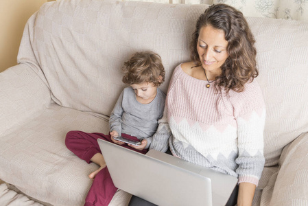 孩子和一个女人在看笔记本电脑和智能手机。