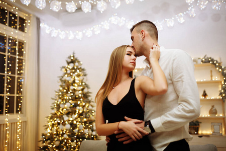 一对相爱的情侣在圣诞树灯旁的沙发上亲吻拥抱。新年之夜。圣诞节。
