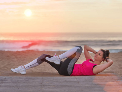 美丽的女人穿着运动服在日落海滩上做瑜伽健身操。运动理念。
