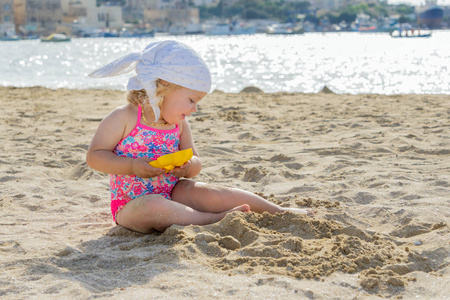 可爱的蹒跚学步的小女孩在白色沙滩上玩耍