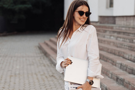 一位穿着牛仔裤和白衬衫的时尚女孩手持笔记本电脑，自由职业者，商务小姐，女性权力概念