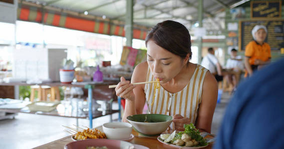 Woman eat boat noodles at outdoor street vendor in Thailand 