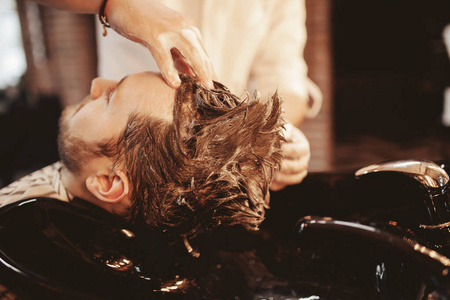 擦水理发店的男人洗头,在水槽里擦洗发水.复古色调照片照片