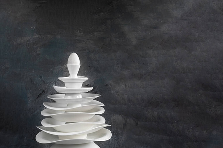 圣诞树用白色盘子做成，在深灰色背景上有一个鸡蛋，复制空间关于餐具厨房餐厅咖啡厅壁纸盘子和餐具的制造的创意概念