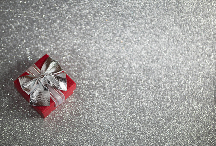 Red gift box with silver bow on silver glitter surface with boke