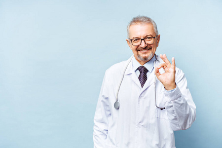 开朗成熟的医生面对镜头医疗保健和药品摆姿势微笑。在蓝色背景下隔离。医生表示可以