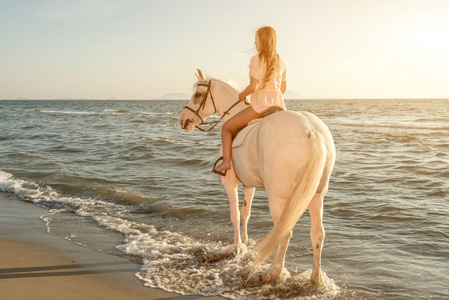 夕阳下沙滩上骑着白马的年轻漂亮女孩
