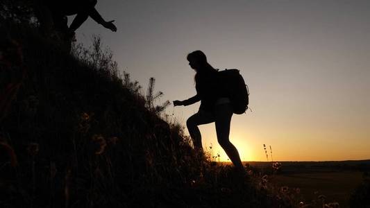 一位女游客拉着一位男性游客的手帮助攀登山顶.