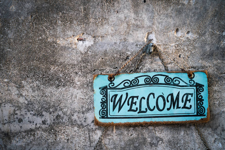 Welcome sign board hanging on stone wall texture background. 