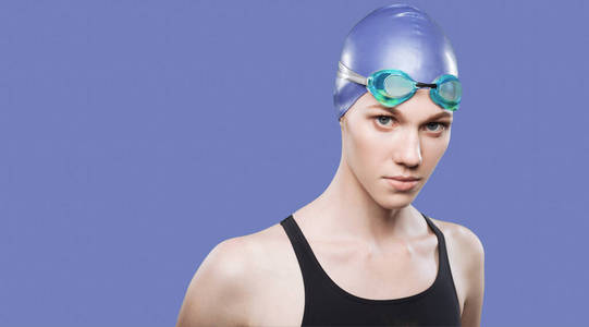 戴泳帽头戴护目镜的女游泳运动员在一个孤立的背景下看着摄像机照片