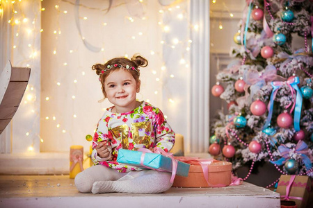 一个小女孩手拿礼物，在圣诞树的背景上梳着两条辫子