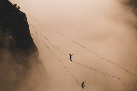 Two highliners are on a line above the cloud. 