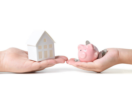 hands holding pink piggy bank and paper model house isolated 