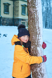 一个可爱的小女孩的冬季肖像。孩子抱着一棵树