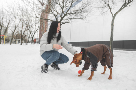 穿着冬装微笑的女人和一只穿好衣服的狗在为一个墙玩耍