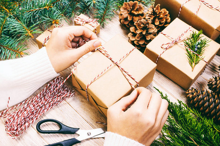 妇女包装圣诞礼物，女孩准备圣诞礼物杉树和松果。手工制作的圣诞装饰木制背景礼物。顶视图，复制空间。色调