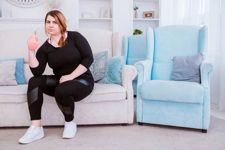 模特——一个胖女人,在家里用哑铃减肥和锻炼.照片