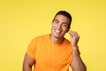 穿着橙色t恤的开朗帅气的男运动员戴着耳机微笑着出门，沿街散步，听音乐，欣赏喜爱的歌曲，为散步创建播放列表，黄色背景