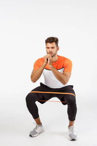 积极专注帅气的运动员使用阻力绳进行下蹲，双脚侧向弯曲伸展设备，坐着并握紧手臂，形成良好的体型，训练理念