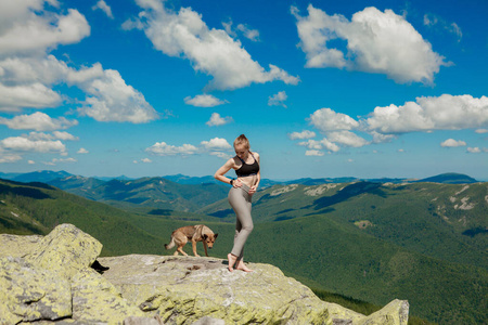 一个女孩抱着狗站在山顶上，张开双臂观看美丽的风景