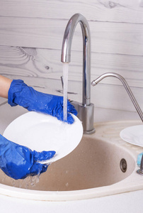 一个戴蓝色手套的女人在流水下洗白色盘子