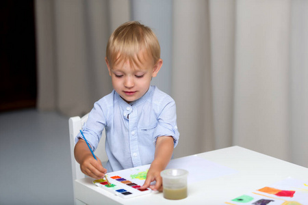 可爱的小男孩坐在桌边用水彩画画