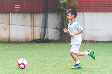 Little Asian boy is running with soccer ball in school football 