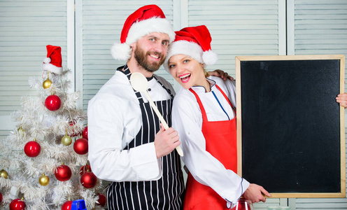 做圣诞大餐。我们家的菜单。圣诞树旁的圣诞老人帽男女厨师手持黑板复制空间。夫妇核对圣诞晚餐的配料表。圣诞食谱概念