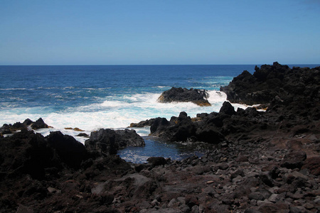 强烈的蓝色海洋和黑色的火山岩图片