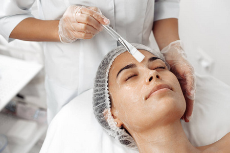 美容师在美容院用刷子在女性脸上涂抹面霜。