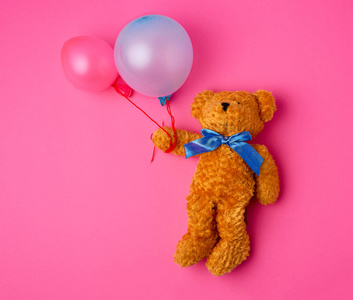 little brown teddy bear holds two inflated balloons on a rope 