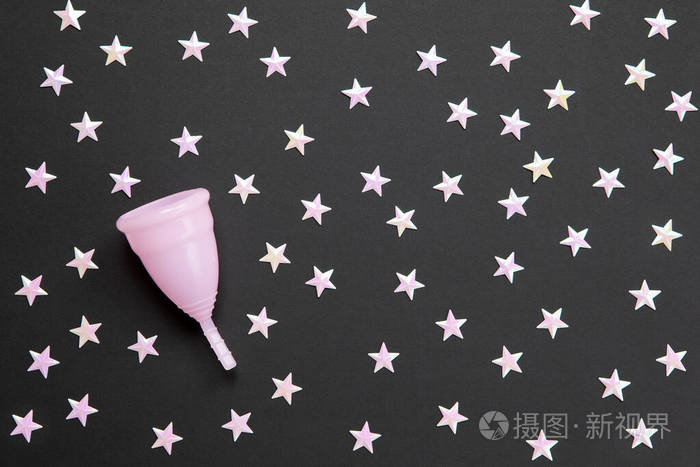 粉红色的月经杯，黑色背景上有许多星星。夜间使用杯子的概念可能性，零浪费，节约，简约。女性卫生用品，平放，复印空间。水平