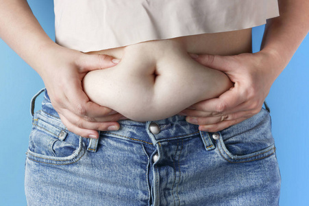 女人的手拿着过多的腹部脂肪，蓝色的背景，减肥的概念