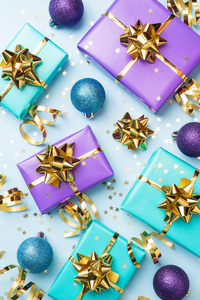 为庆祝圣诞节和新年的平整背景。礼品盒是紫色和绿松石色，蓝色背景上有金色丝带蝴蝶结和五彩星星。俯视图