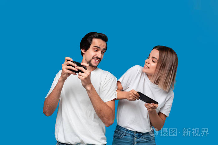这对夫妇穿着白色t恤在蓝色背景下孤立地站着用手机玩游戏