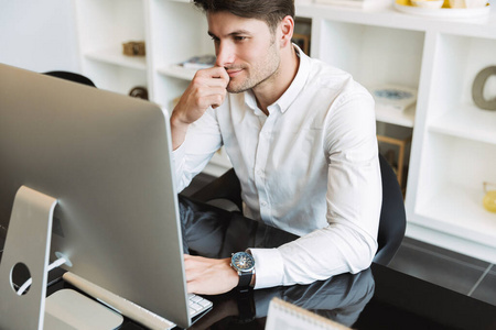 Image of smart businesslike man sitting at table and working on 