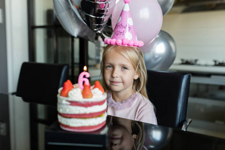 室内拍摄的金发碧眼的小女孩吹灭蜡烛，庆祝6岁生日，穿上时髦的衣服，有兴奋的表情。快乐童年观