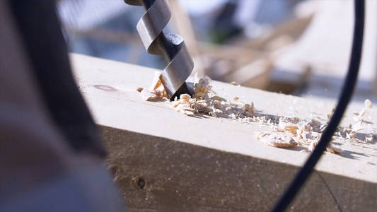 木工用钻在木梁上打孔，手工概念，木工。削减。木刨花工作钻特写。