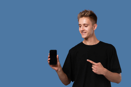 穿着黑色T恤的少年拿着智能手机，指着蓝色背景上隔离的屏幕