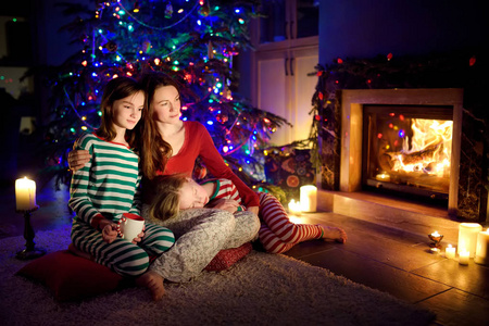 圣诞前夜，幸福的年轻母亲和女儿们坐在壁炉旁，在一个舒适黑暗的客厅里度过了美好的时光。在家庆祝圣诞节。
