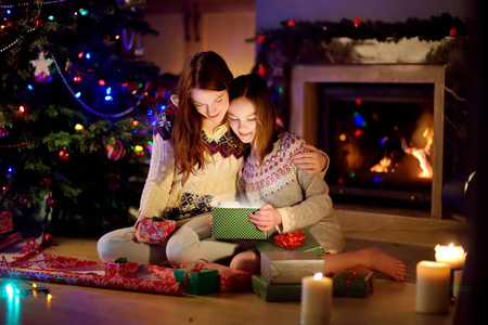 平安夜，在一个舒适黑暗的客厅里，快乐的年轻母亲和她的小女儿在壁炉旁打开一份神奇的圣诞礼物。