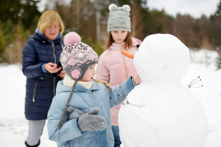 可爱的小女孩和她们的奶奶在后院堆雪人。孩子们在雪地里玩耍。