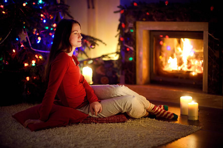 圣诞夜，一个快乐的年轻女子，在一个舒适黑暗的客厅里坐在壁炉旁度过了一段美好的时光。在家庆祝圣诞节。