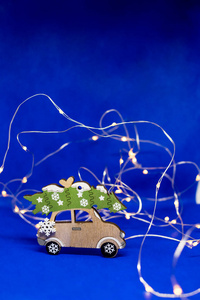 圣诞玩具车，蓝色背景上有圣诞树花环。木制老爷车。圣诞节或新年最少概念。微型汽车。假日背景。快乐新年。复制空间