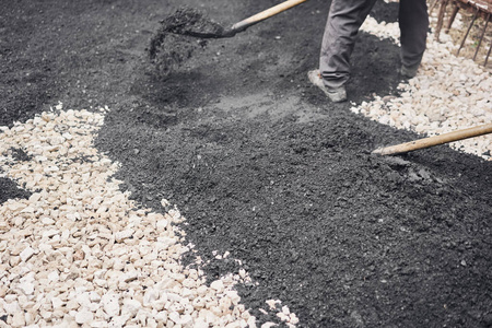 在碎石上铺设新的沥青，覆盖坑。工人们拿着铲子，用沥青琵琶打磨光滑的热沥青。
